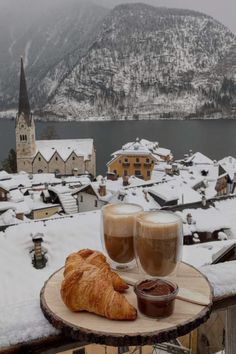 two glasses of coffee and croissant on a table with snow covered mountains in the background