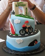 a man taking a picture of a birthday cake with a motorcycle theme on the front