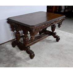 an old wooden table with carved legs on carpeted floor