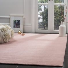 a pink area rug in front of a window with white vases on the floor