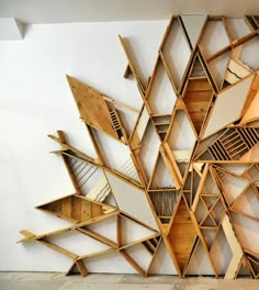 a large wooden sculpture with multiple pieces of wood stacked on top of each other in front of a white wall