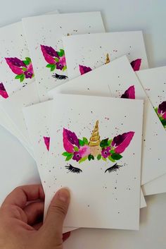 a hand is holding some cards that have unicorns on them and flowers in the middle