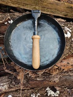 a frying pan with a wooden spatula in it on the ground next to logs