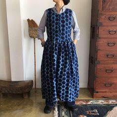 a woman standing in front of a dresser wearing a blue dress with circles on it