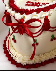 a large white cake with red decorations on it's sides and ribbon around the edges