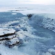 people are standing at the edge of a frozen waterfall and looking out over the water