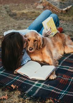 a woman laying on the ground reading a book with her dog