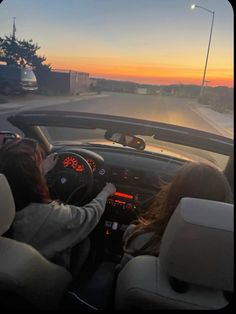 two people in a car driving down the road at sunset or dawn with their hands on the steering wheel