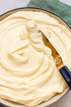 a pan filled with white frosting next to a blue spatula