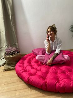 a woman sitting on a pink bean bag chair talking on her cell phone and smiling