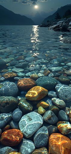 some rocks and water with the moon in the sky above them on a lake shore