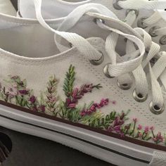 a pair of white shoes with flowers painted on the side and laces around them