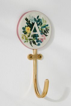 a gold coat hook with a floral monogrammed letter on the front and bottom