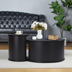 two black tables with white flowers on them in front of a couch and coffee table