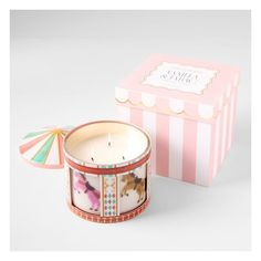 a candle in a pink and white box next to a small carousel themed candle holder