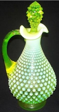 a green and white glass vase sitting on top of a table next to a black background