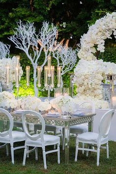 a table with white flowers and candles is set up for an outdoor wedding reception in the grass