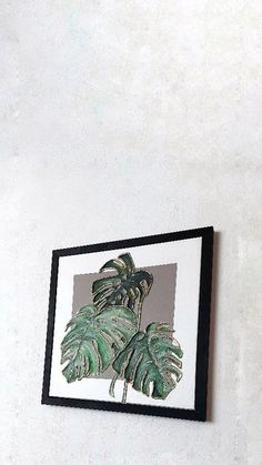 a white wall with a black frame hanging on it and a green plant in the corner