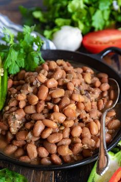 a black plate filled with beans and lettuce on top of a wooden table