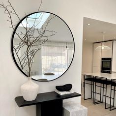 a round mirror hangs on the wall above a table with stools and a vase