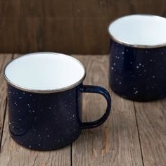 two black and white coffee mugs sitting on top of a wooden table next to each other