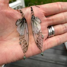 These forest fairy grunge earrings can only be described as enchanting. Measuring 2" in length with a 2.25" drop, they delicately sway, crafted from translucent printed plastic adorned with olive green accents and a subtle dusting of golden glitter, adding a touch of sparkle.An olive green opaque crystal and multi-colored metallic luster crystal dangle from twisted wire branches in your choice of antique bronze or gold. These enchanted fairy wing earrings are suspended on either antique bronze o Gothic Accessories Fairy, Botanical Metal Jewelry, Magical Accessories Earrings, Fantasy Crystal Earrings, Fairy Grunge Jewelry Rings Size 6, Grunge Jewelry Earrings Gold, Cheap Green Whimsical Flower Earrings, Magical Accessories Not On The High Street, Hipiee Earrings