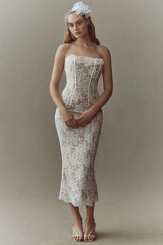 a woman wearing a white dress and headpiece standing in front of a gray background