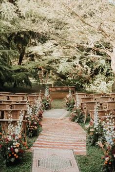 an outdoor ceremony setup with wicker chairs and flowers on the aisle, surrounded by greenery