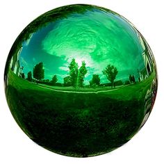 a green glass ball with trees in the reflection on it's surface, reflecting sky and clouds