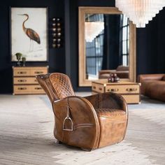 a brown leather chair sitting on top of a wooden floor next to a mirror and dresser