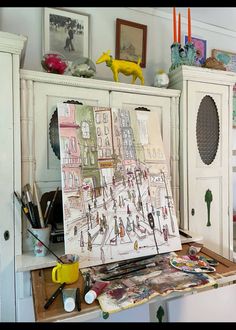 an artist's easel sitting on top of a table covered in art supplies