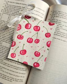 an open book with cherries on it and a tag attached to the page that says i love you