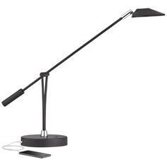 a black desk lamp with a cell phone on the charger next to it and a white background