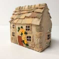 a small house made out of clay with flowers painted on the roof and windows, sitting on a white surface