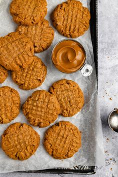 peanut butter cookies on parchment paper with spoons and jar of peanut butter next to them