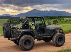 an old jeep is parked on a dirt road in front of some mountains and grass