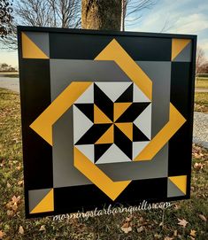 a black, yellow and white quilt is on display in the grass near a tree