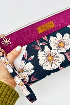 a woman holding a pink and black flowered wristlet bag in her right hand