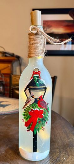 a glass bottle with an image of a bird and christmas wreath on it sitting on top of a wooden table