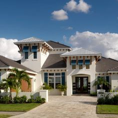 a large white house with blue shutters and palm trees in the front yard on a sunny day