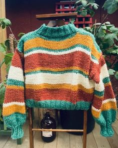 a colorful sweater sitting on top of a wooden chair next to a potted plant