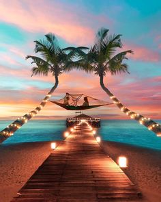 a wooden walkway leading to the beach with lights on it and palm trees in the foreground