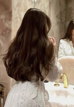 the woman is brushing her long hair in front of the mirror and looking at herself in the mirror