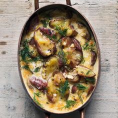 a dish filled with potatoes and herbs on top of a wooden table