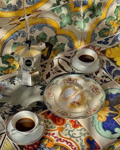 two plates with pastries and cups of coffee sit on a colorful table cloth, next to an umbrella