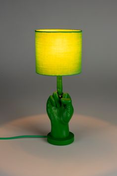 a green table lamp with a yellow shade on it and a hand holding the base