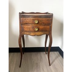 an old wooden table with two drawers and gold knobs on the top, against a white wall