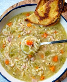 a bowl of chicken noodle soup with two slices of bread on the side and a spoon in it