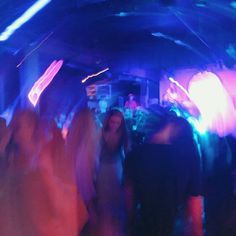 blurry image of people dancing in a club at night with neon lights on the ceiling