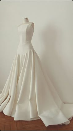 a white wedding dress on display in front of a white wall and wood flooring